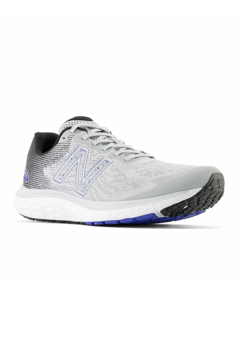 Zapatilla de running New Balance en gris y negro con suela blanca y acentos azules, vista lateral sobre un fondo blanco.