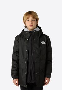 Black insulated jacket with a hood, featuring a zip and snap closure, two front pockets, and a gray fleece lining. Logo on the chest.