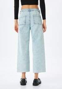 Celana culotte denim biru muda dengan pinggang tinggi, kaki lebar, dan dua kantong belakang. Hemnya mentah dan bahan kainnya memiliki tekstur pudar.