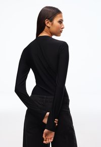 Hosszú ujjú fekete body sima anyagból, testhezálló szabással és magas nyakrésszel, magas derekú sötét farmerrel párosítva.