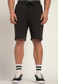 Schwarze Baumwollshorts mit einem elastischen Bund und Kordelzug. Kombiniert mit schwarz-weißen Sneakers und gestreiften Crew-Socken.