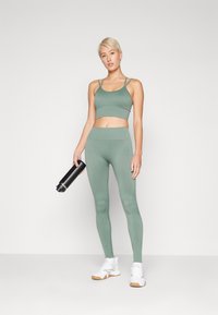 Conjunto deportivo ajustado en verde con un top corto y leggings de cintura alta, acompañado de zapatillas deportivas blancas y una botella de agua negra.