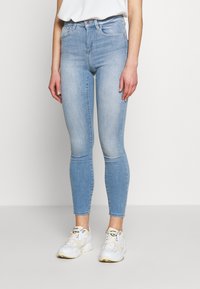 Slim-fit, ljusblå jeans med subtil blekning, fem fickor och midjehöjd; matchat med vita sportskor.