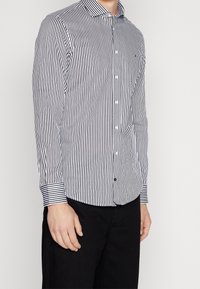 Camicia a maniche lunghe a righe bianche e blu navy con colletto botton-down, orlo curvo e polsini a contrasto. Il materiale sembra liscio con una vestibilità su misura.