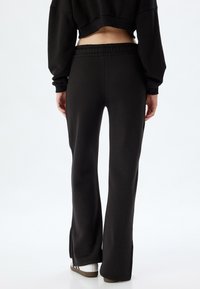 Zwarte flared sweatpants met een elastische tailleband, voorzien van een zachte textuur en zijsplitten aan de zoom voor meer bewegingsvrijheid.