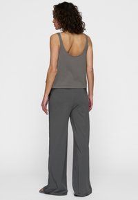 Canotta grigia in cotone con schiena ampia e vestibilità morbida, abbinata a pantaloni grigi a gamba larga coordinati. Design minimalista senza motivi o accessori visibili.