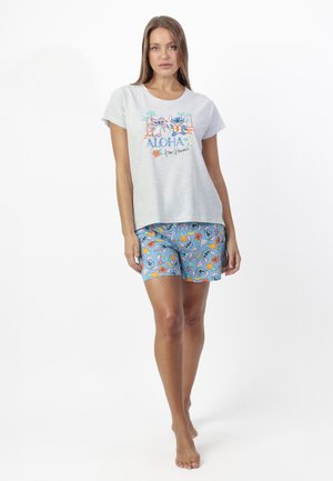 Mujer con camiseta gris claro con personajes de Stitch y texto "ALOHA desde Hawaii", combinada con pantalones cortos azules con frutas coloridas y caras de Stitch.