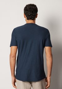 Marinblå t-shirt med kort ärm gjord av mjukt, texturerat tyg. Har en rundad halsringning och en något rundad nederkant, med en avslappnad passform.