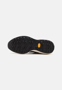 Black rubber shoe sole with a rugged tread pattern; features a yellow Vibram label on the heel for enhanced grip and durability.