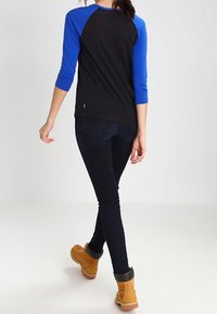 Svart och blå tröja med trekvartslång ärm, kombinerad med mörka tighta jeans och bruna stövlar, med rundad fåll och kontrasterande ärmdesign.