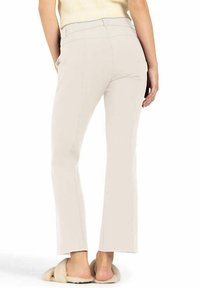 Light beige pants with a tailored fit, straight legs, and subtle seams. Worn with fuzzy slippers, showing the hem and soft texture.