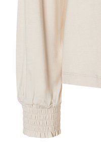 Lange beigefarbene Ärmel mit gerafftem elastischem Bund, aus weichem, leichtem Stoff gefertigt. Nahtdetails sind in der Nähe des Saums und am Handgelenk sichtbar.