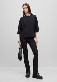 T-shirt nera oversize con logo bianco sul colletto, abbinata a pantaloni neri attillati e stivali platform neri chunky. Borsa nera con tracolla.
