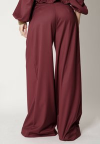 Spodnie o szerokich nogawkach w głębokim burgundowym kolorze. Gładka tkanina z płynącym krojem i wysokim stanem. Posiada kieszenie z tyłu dla lepszej funkcjonalności.