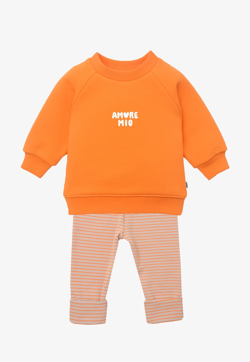 Oranger Baumwoll-Sweatshirt mit weißem "AMORE MIO"-Text, kombiniert mit beige-orange gestreiften Leggings mit aufgerollten Säumen.