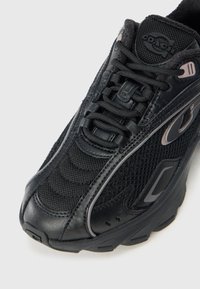 Μαύρο αθλητικό παπούτσι με επάνω μέρος από πλέγμα και δέρμα, υφή λεπτομέρειας, αντίθετες γκρι λεπτομέρειες και επενδεδυμένη σόλα.