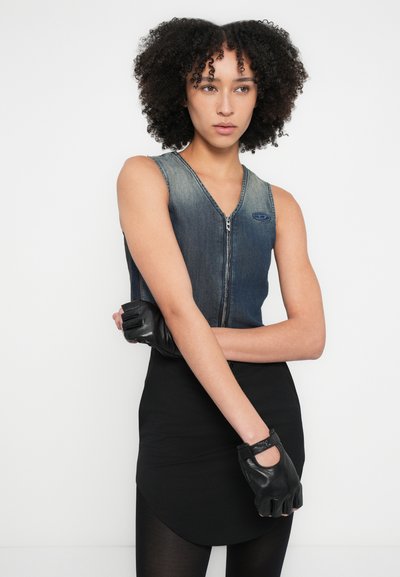 Haut sans manches en denim avec un col en V, fermeture éclair à l'avant et coutures bleues, associé à une jupe noire ajustée et des gants noirs sans doigts.