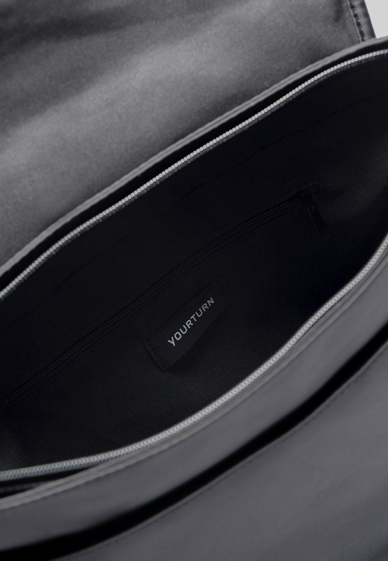 Interior negro de una bolsa, con un forro texturizado y un bolsillo con cremallera. Etiqueta "TU TURNO" visible en el lateral.