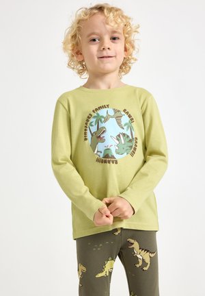 Lichtgroen shirt met lange mouwen en een dinosaurusafbeelding, gecombineerd met donkergroene legging bedrukt met dinosaurussen.