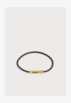 Braccialetto in pelle intrecciata nera con una chiusura cilindrica in oro incisa con la parola "BOSS" in lettere nere.