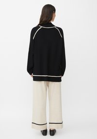 Maglione nero oversize con dettagli crema, abbinato a pantaloni beige a gamba larga con bordi neri. Tessuto morbido e liscio.