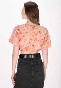 Persikkakukkainen lyhythihainen crop-top, jossa on puffihihat ja laskostettu helma, yhdistettyinä korkeavyötäröisiin mustiin farkkuhameisiin, joissa on takataskut.