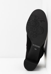 Chaussure en cuir suédé noir avec une semelle texturée. La semelle présente des motifs en relief et le nom de la marque "Peter Kaiser" avec la taille "4½" imprimée.