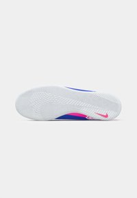Kék és rózsaszín Nike sportcipő fehér háttérrel, oldalról látható, ahol a talp vékony, textúrázott fehér, és a saroknál rózsaszín Nike pipa található.