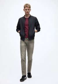 Melnā bombere, bordo krāsas T-krekls, gaiši pelēkas džinsa bikses un melni sporta apavi. Gluda auduma un pieguloša dizaina jaka ar ribotām aprocēm un apakšmalu.