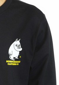 Musta pitkähihainen paita, jossa on värikäs sarjakuvahahmo -kuvio vasemmassa rinnassa ja "NORDICBUDDIES CLOTHING CO." -teksti sen alla.