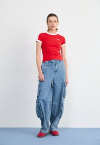 Red t-shirt with white sleeves and logo, paired with oversized light blue cargo jeans featuring multiple pockets, worn with red shoes.