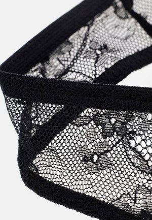 Bande de tissu en dentelle noire avec des motifs floraux et des bords festonnés sur fond blanc.