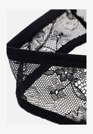 Bande de tissu en dentelle noire avec des motifs floraux et des bords festonnés sur fond blanc.