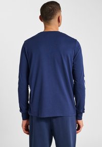 Marinblå långärmad skjorta med rund halsringning, tillverkad av glatt tyg; har kontrasterande vita detaljer på ärmarna och en avslappnad passform.