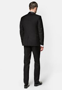 Czarny garnitur o dopasowanym kroju, z pojedynczym rozcięciem z tyłu, długie rękawy z białymi mankietami koszuli, gładka tekstura, w połączeniu z czarnymi eleganckimi butami.