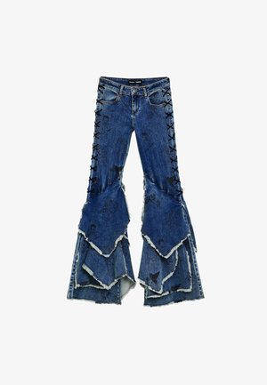 Jeans de mezclilla azul de campana con diseño de volantes en capas, que presentan detalles de encaje negro en los lados y bordes deshilachados.