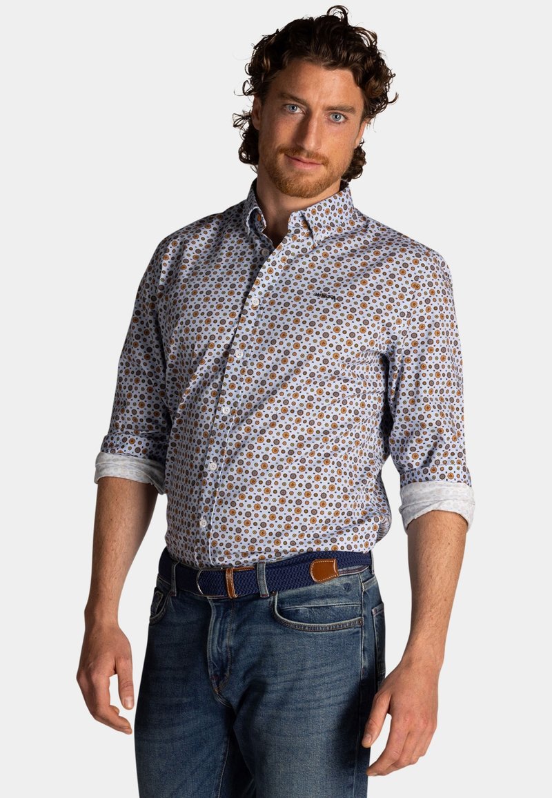 Overhemd met knopen, gekenmerkt door een witte achtergrond met bruine cirkelvormige patronen, opgerolde mouwen en een klassieke kraag, gecombineerd met blauwe jeans en een gevlochten riem.