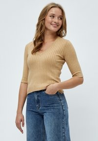Top en tricot côtelé beige avec un décolleté en V et des manches courtes. Associé à un jean en denim bleu taille haute. Design simple avec une silhouette ajustée.