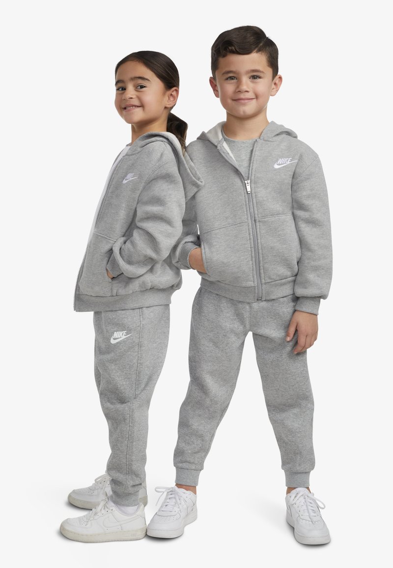 Grå huvtröja och joggingbyxor i bomullsblandning med frontdragkedja, sidofickor och vita logotypdetaljer. Kombinerat med vita sneakers.