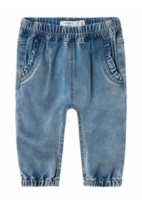 Los pantalones de mezclilla azul cuentan con una cinturilla elástica, bolsillos laterales y puños fruncidos en los tobillos. La tela tiene una textura desgastada.