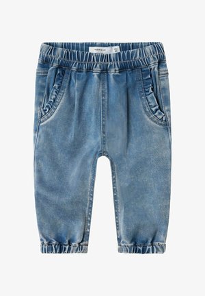 Niebieskie dżinsy mają elastyczny pas, boczne kieszenie i marszczone mankiety u kostek. Materiał ma wyblakłą teksturę.