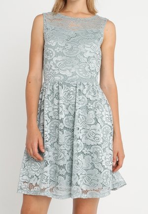 Sleeveless light gray lace dress with floral patterns, fitted bodice, sheer neckline, and flared skirt worn by a standing person.