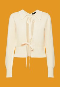 Cardigan en maille crème à manches longues, col large et deux liens à l'avant sur un fond orange uni.