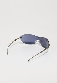 Lunettes de soleil avec des verres violets, forme ovale élégante, et branches en métal courbées et torsadées. Les plaquettes de nez en acétate assurent un maintien sécurisé.
