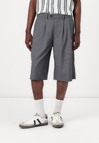 Gray pleated shorts with a lightweight, textured fabric, featuring a waistband and side pockets. Worn with white socks and sneakers.