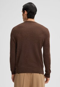 Pull en tricot marron à manches longues, col rond et poignets côtelés. Texture douce et coupe légèrement ample, se terminant à la taille.
