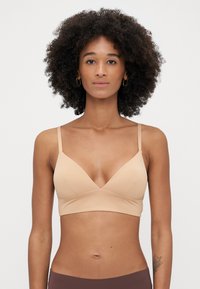 Beige langaton bralette, jossa on V-mallinen dekoltee, säädettävät ohuet hihnat ja sileä, joustava kangas. Varustettu tiukalla alareunalla.