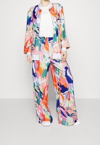 Chándal colorido que incluye una chaqueta con cremallera y pantalones de pierna ancha, confeccionado en una tela suave con patrones abstractos en rosa, azul, verde y naranja.