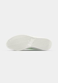 Fehér sneaker talp halszálka mintával, zöld kiegészítőkkel. Az anyag gumiszerűnek tűnik, textúrázott részletekkel és logóval az oldalán.