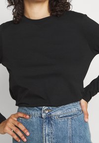 Svart långärmad T-shirt i bomull med rund halsringning, ihop med högmidjade blå denimjeans med en framknapp och ficka.